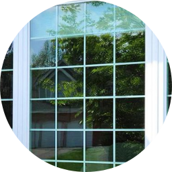 Grid-Style Double Pane Window Reflecting Outdoor View Close-up of a white-framed window with a grid design, showing a clear reflection of trees and a suburban house with a double garage, captured in natural daylight.