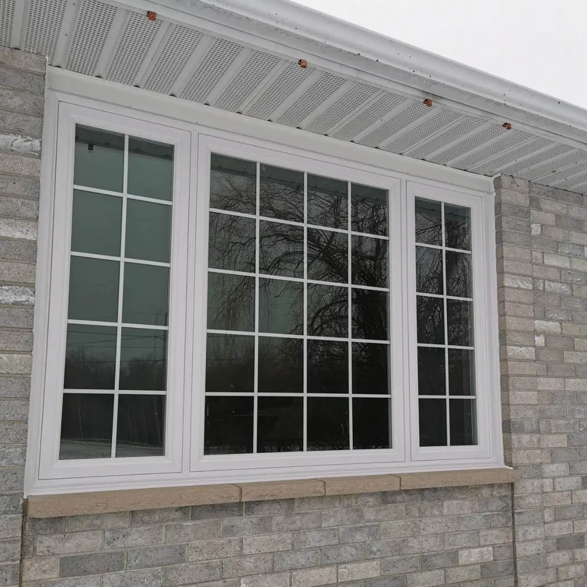 Newly installed white-framed triple-pane window with grid design on a brick exterior wall.