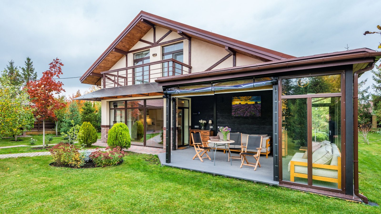A modern two-story home with large energy-efficient windows and a glass-enclosed patio, surrounded by a well-maintained garden and vibrant autumn trees.