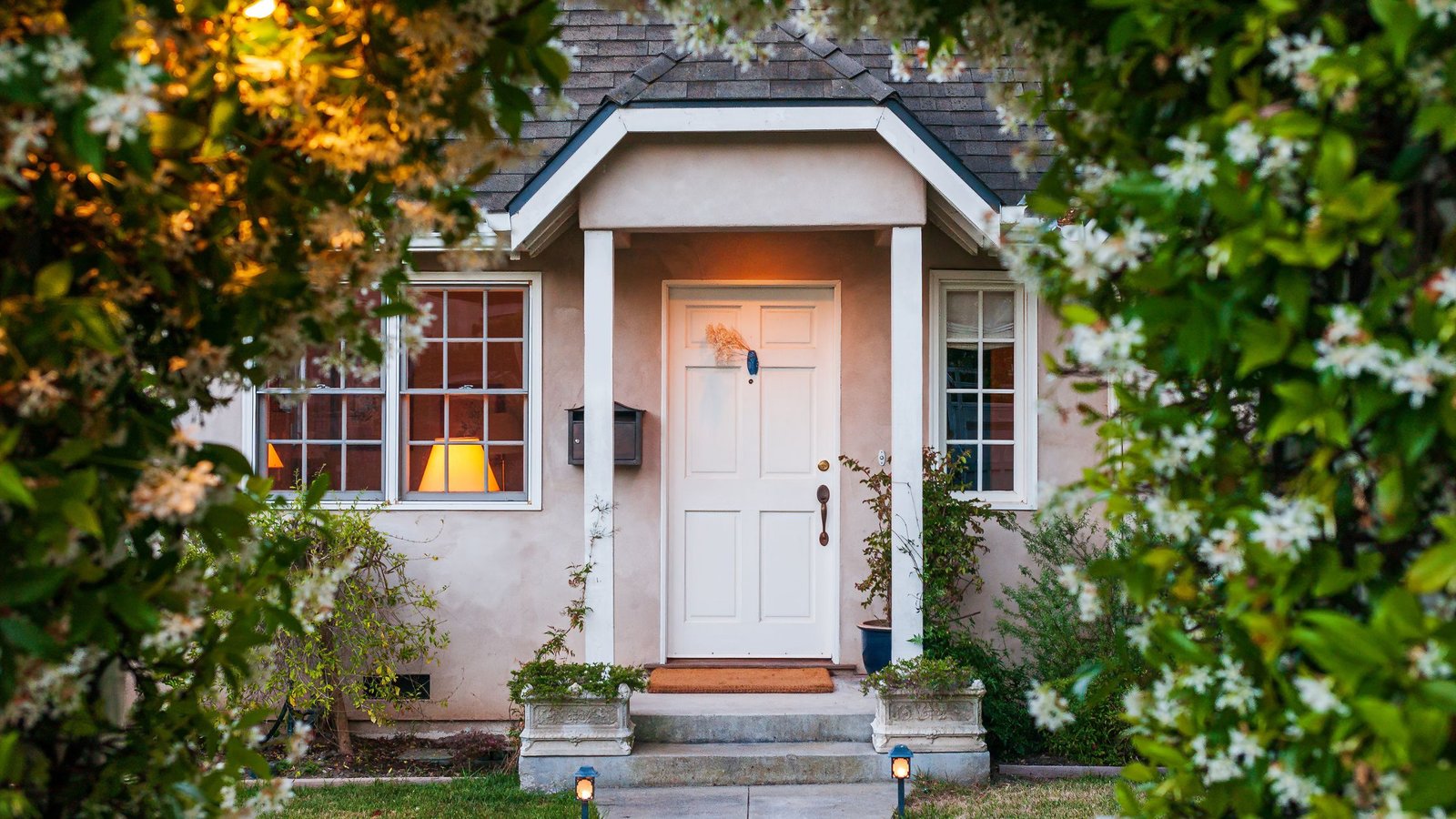 Charming home entrance framed by blooming greenery, featuring a white front door with sidelights, illustrating How to Choose Durable Entry Doors for long-lasting curb appeal.