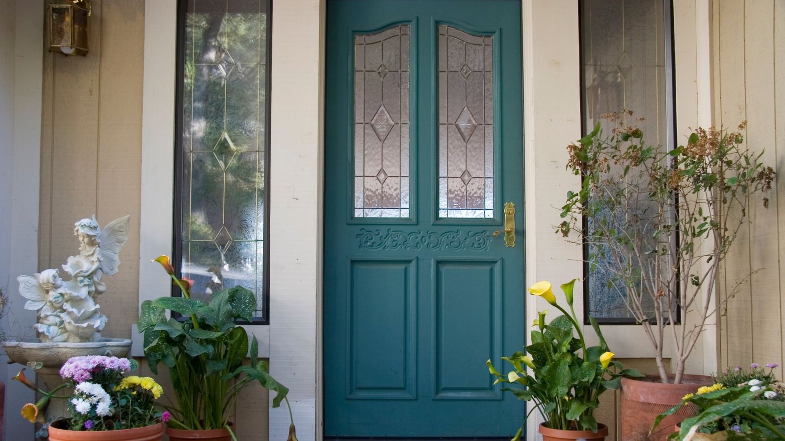 Teal front door with decorative glass panels, surrounded by sidelights and potted plants, illustrating a home entryway when deciding to repair or replace a broken door.