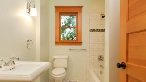 Small bathroom with a bathtub, white tile shower, and a wooden-framed window above the toilet, showcasing a window type for showers that provides natural light while maintaining privacy.