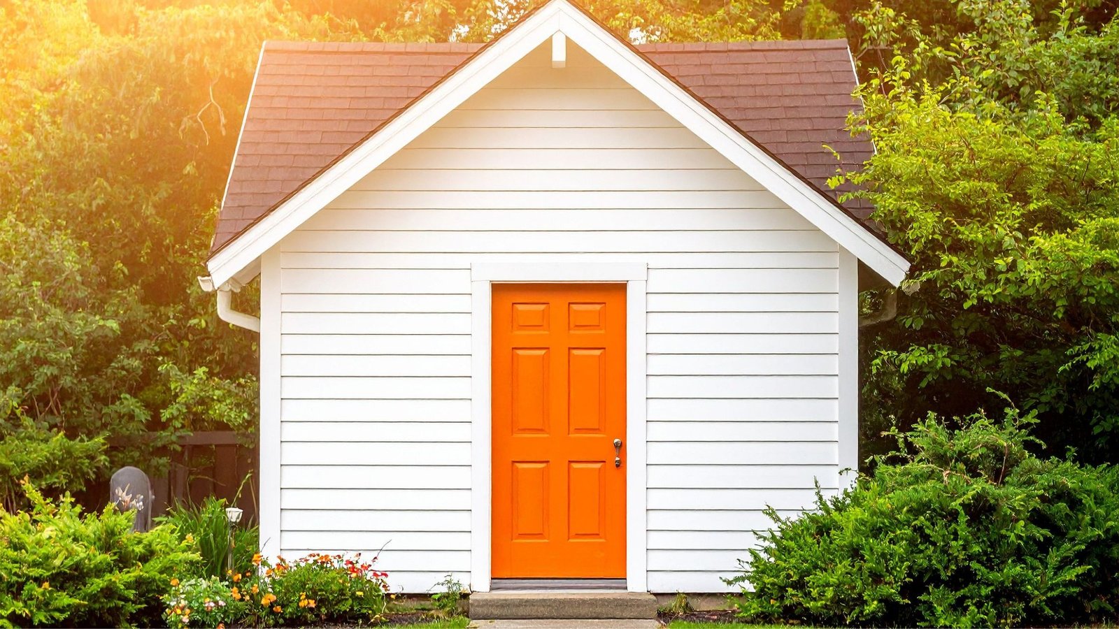 White house with bright orange front door surrounded by greenery, illustrating curb appeal and energy efficiency as part of signs your door needs replacement in Vaughan.