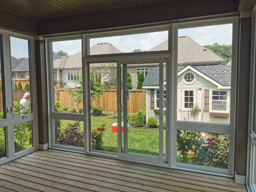 Garden Doors with Glass Panels – Elegant Backyard Access with Screened Porch View White garden doors with large glass panels opening to a backyard with green lawn, garden shed, and wooden deck flooring in a screened porch.
