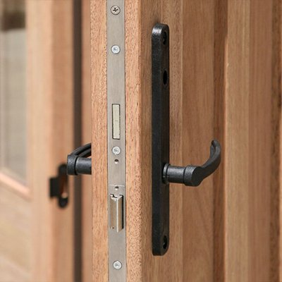 Close-up of a black multi-point lock system on a wooden door, showing detailed latch and handle mechanism.