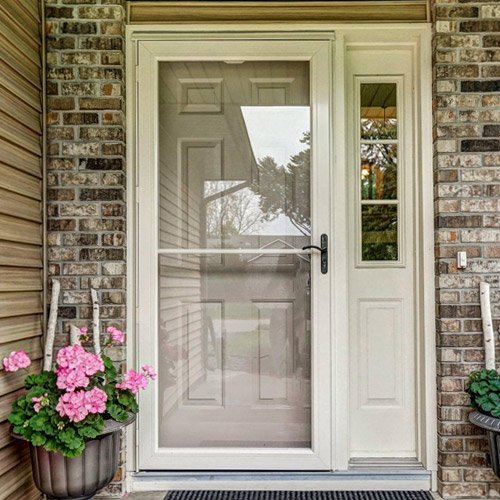 Full-View White Storm Door for Front Entry – Durable Exterior Door with Glass Panel White storm door with full-view glass panel installed on a brick house entryway with a side window and pink flowers in planters.